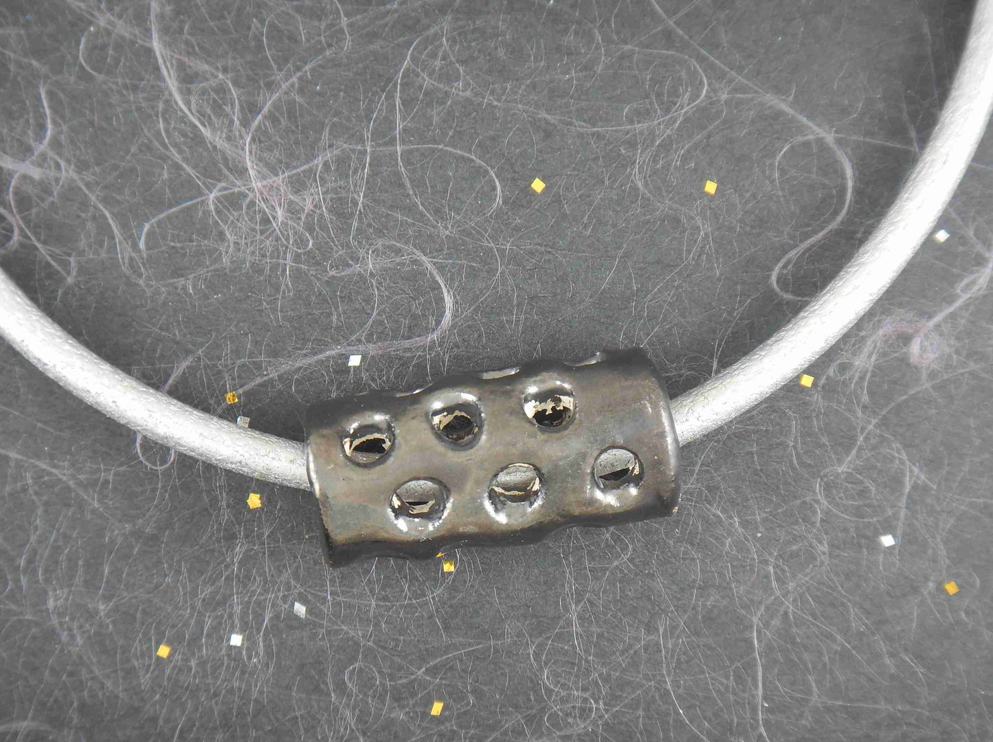 Collier tour de cou avec cylindre de céramique nickel noir fait main à Montréal, motifs de trous, cordon de cuir argenté métallisé, fermoir acier inoxydable