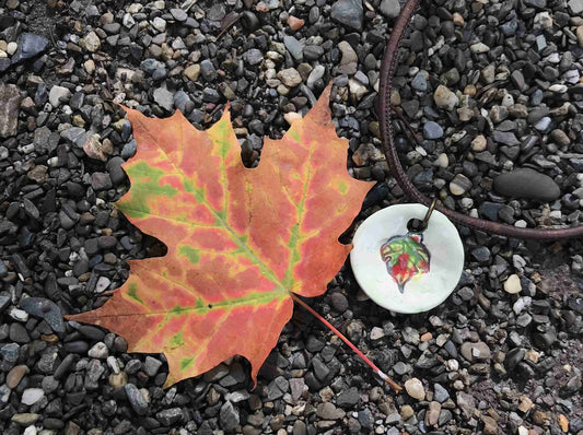 18-inch necklace with off-white ceramic medallion pendant handmade in Montreal, red-green-yellow leaf pattern, chocolate brown cork cord, aluminum ring, stainless steel clasp