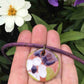 Collier 18 po à pendentif médaillon de faïence terracotta avec motif fleuri blanc-vert-violet fait à la main à Montréal, cordon de liège violet, anneau aluminium, fermoir acier inoxydable
