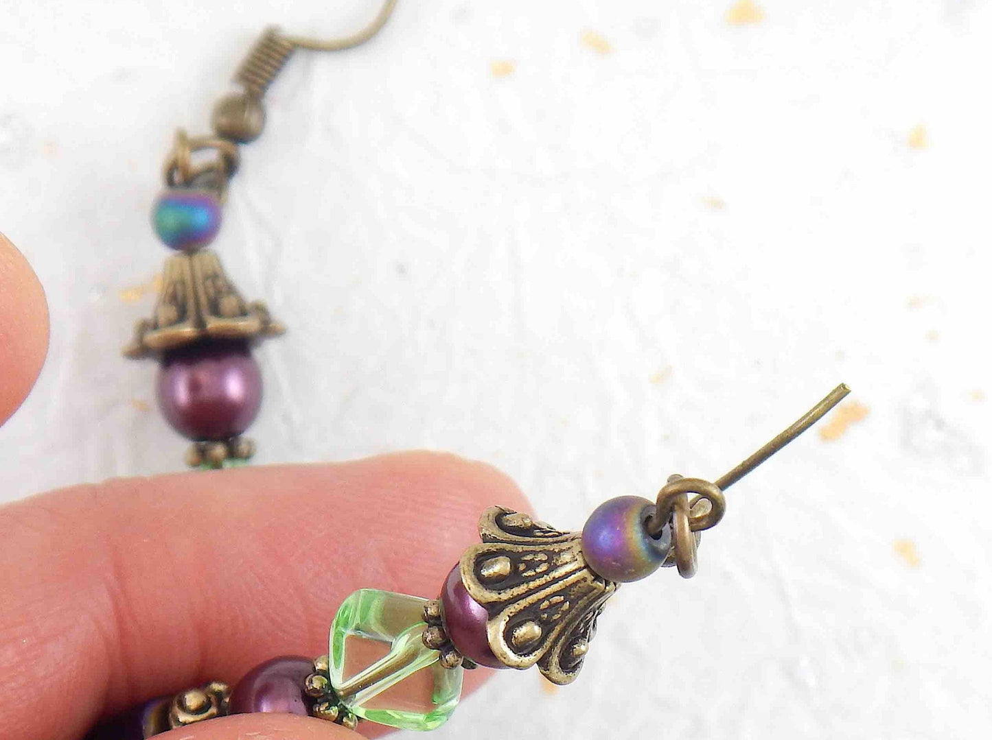 Long layered earrings with metallic violet cubes, plum balls, green lozenges, violet crystals, brass caps, brass hooks