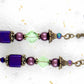 Long layered earrings with metallic violet cubes, plum balls, green lozenges, violet crystals, brass caps, brass hooks