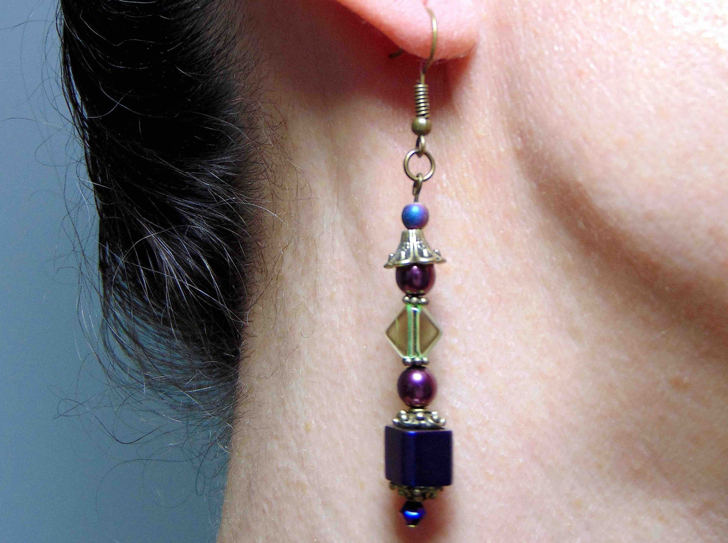 Long layered earrings with metallic violet cubes, plum balls, green lozenges, violet crystals, brass caps, brass hooks