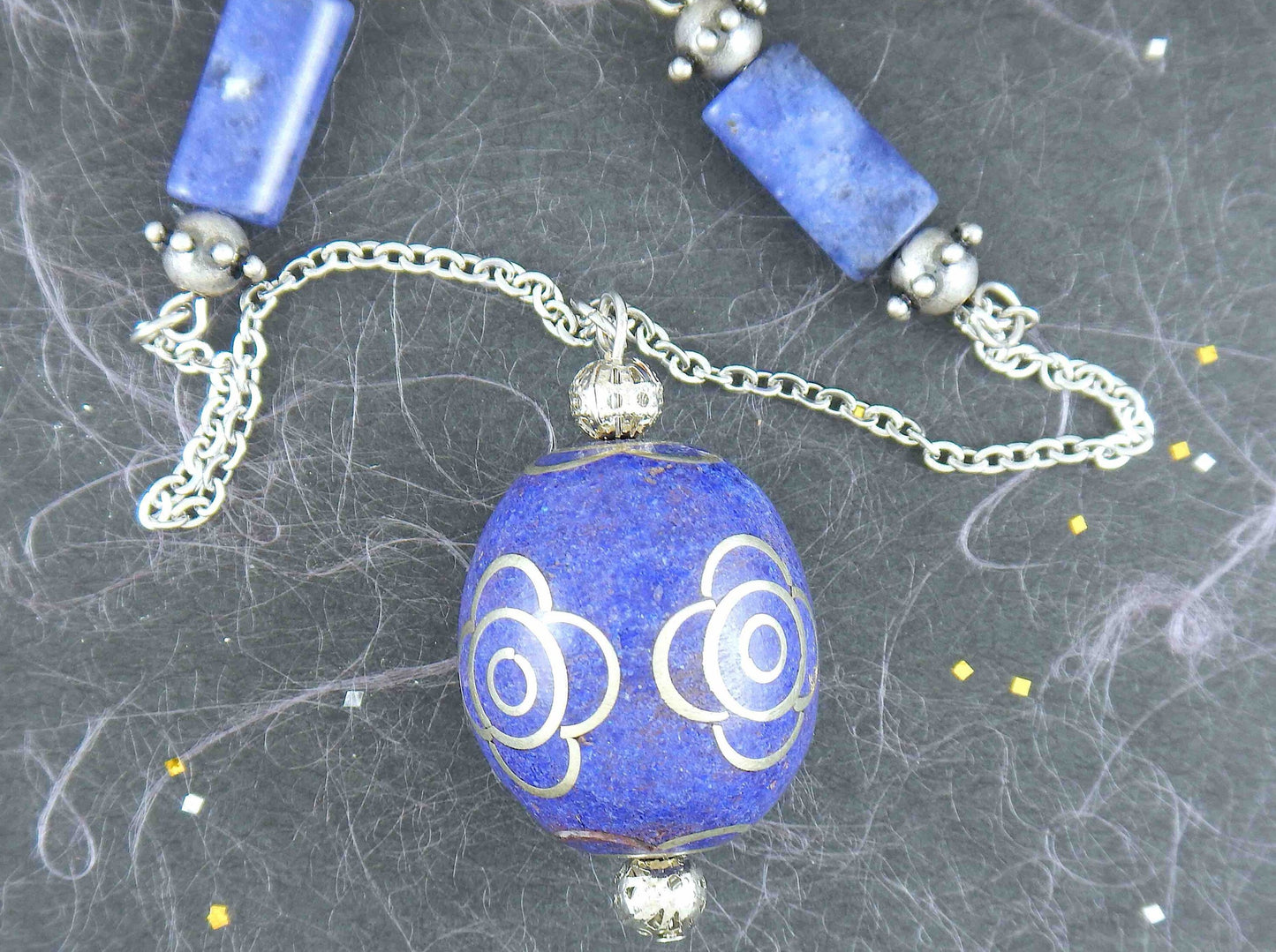 31-inch necklace with deep indigo blue egg-shaped resin Tibetan bead, pewter flower details, sodalite, stainless steel chain