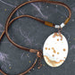 17-inch necklace with matte white and caramel jasper pendant on brown leather cord, antique glass cylinder beads, copper clasp