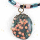 20-inch forest green oval jasper pendant with coral pink dots, black satin cord, antique glass cylinder beads, copper clasp
