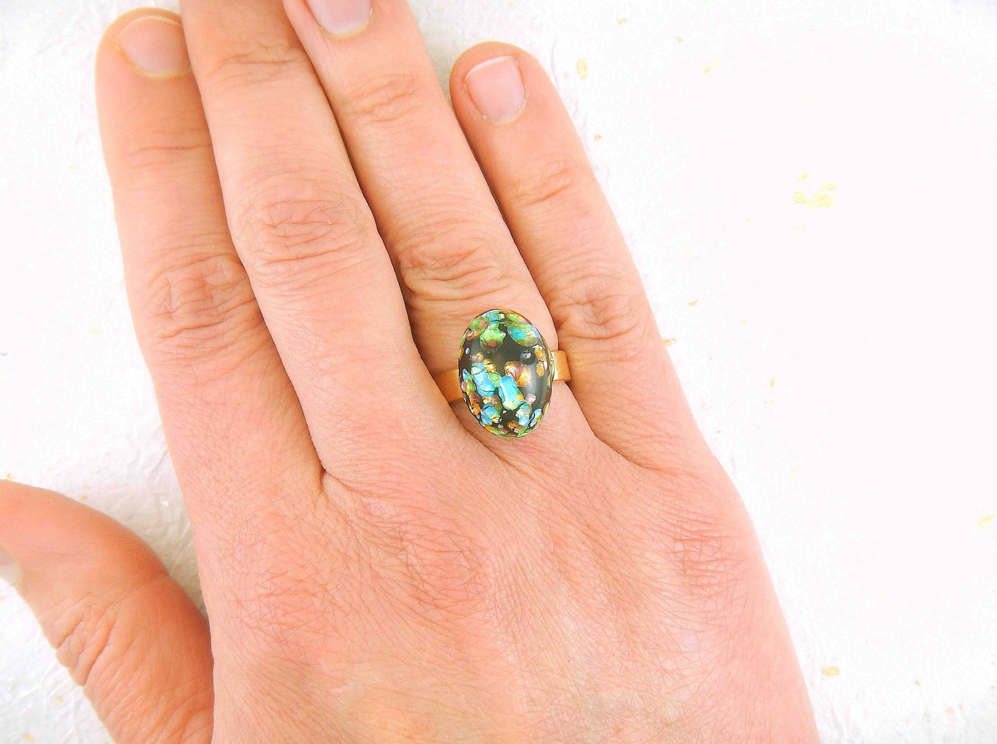 Finger ring with black oval vintage glass cabochon, blue-green-gold speckled, gold-toned stainless steel adjustable base