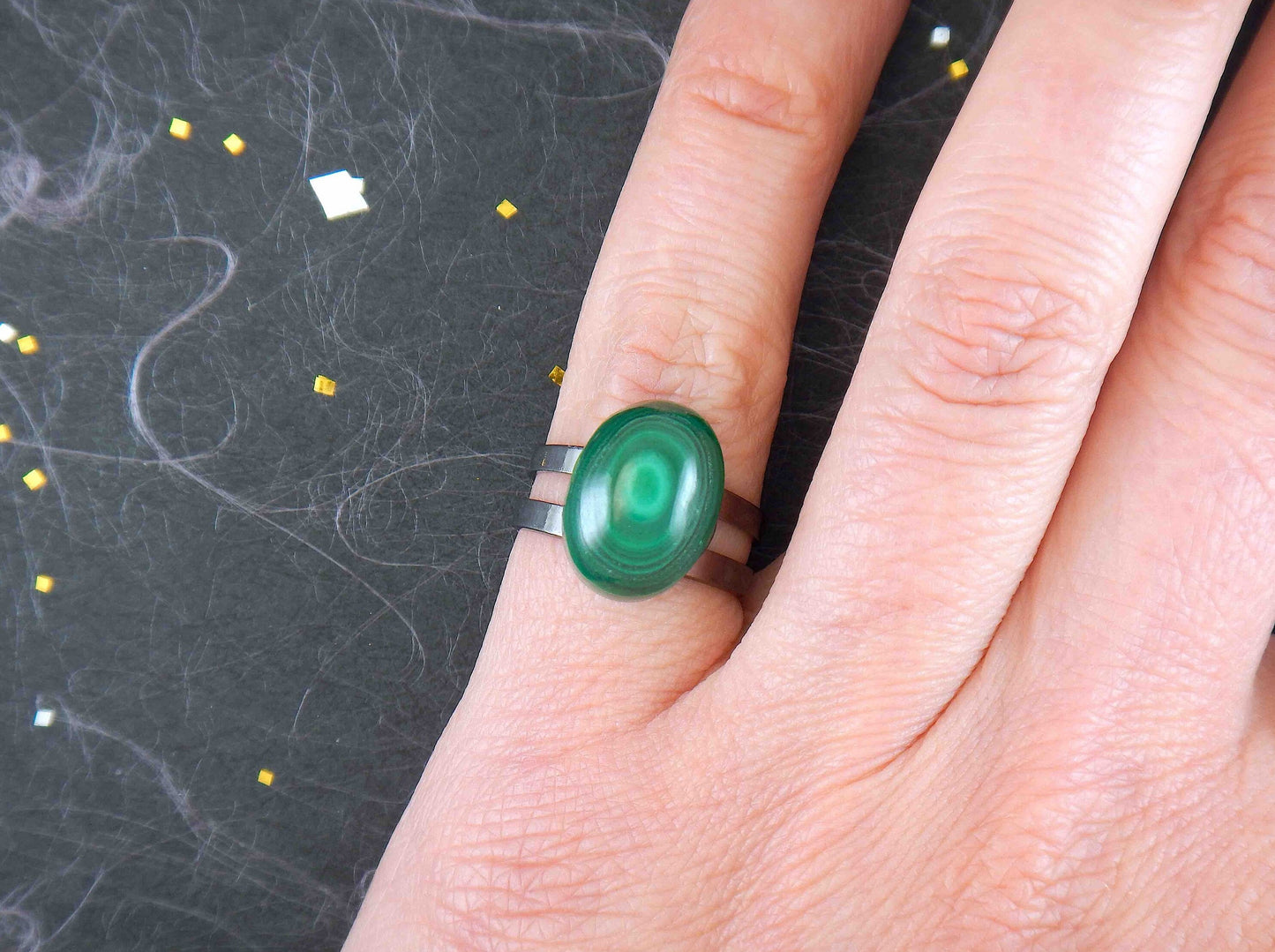 Finger ring with small oval malachite stone cabochon, concentric dark and light green rings, black nickel metal adjustable base (US 5-6)